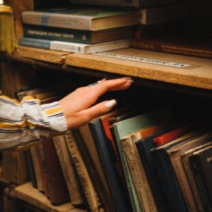 pexels photo 11870983 woman hand over books on shelves